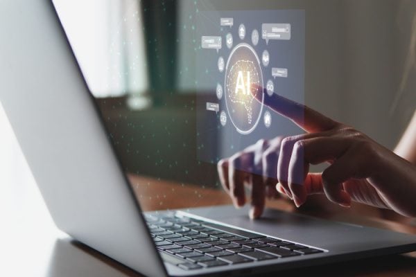 person working at a laptop and touching a projected screen with an AI icon on it