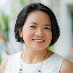 Lai Han Sam PCC headshot photo, smiling woman with short dark hair wearing a white top in front of blurred greenery