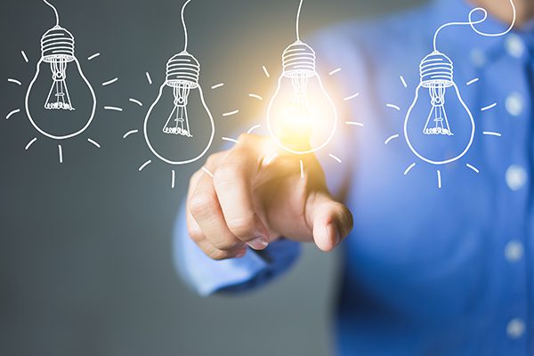 Person touching an overlayed drawing of a lightblub with it emmitting light amongst other unlit lightbulb drawings