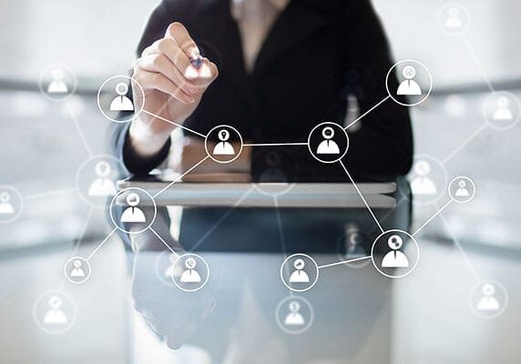 woman at table using pen to connect people icons on transparent screen