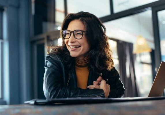smiling woman looking to her right while sitting at a table with her laptop
