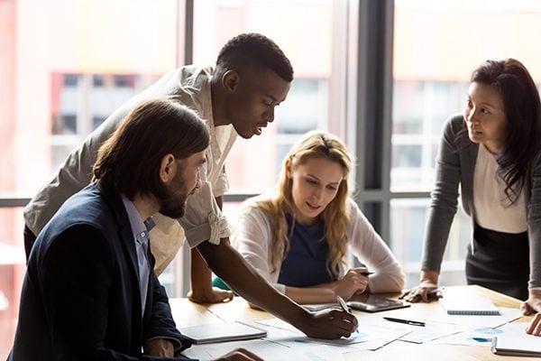 four people meeting around a table with one making marks on a piece of paper