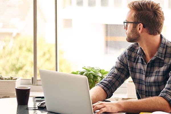 coach procrastinating by looking out of a window while his hands are on a laptop keyboard