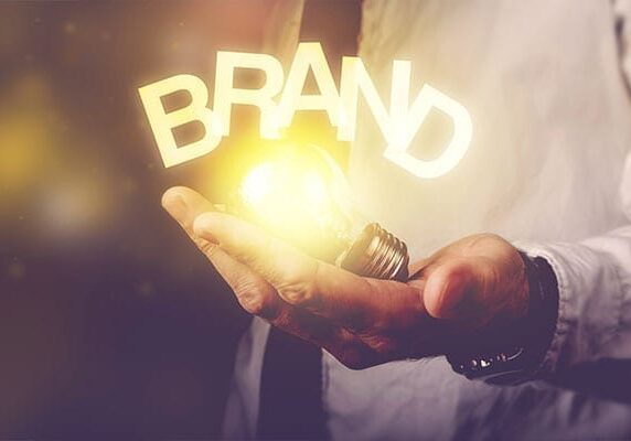 person holding a lit lightbulb in their hand with the word BRAND over it