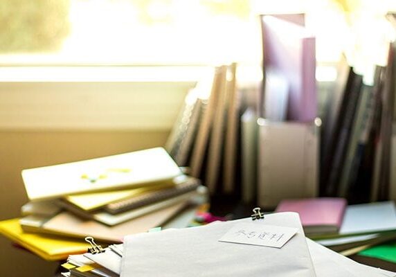 disorganized desk with piles of papers and files