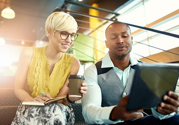 coach selling his coaching services to a woman who is holding a notebook and a coffee cup
