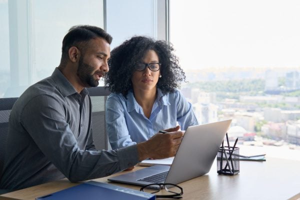 man showing a woman something on a laptop at a desk and explaining what is on the screen