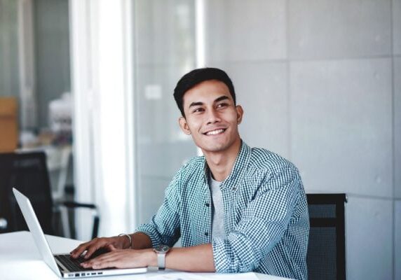 man smiling while working on a laptop and looking to his left