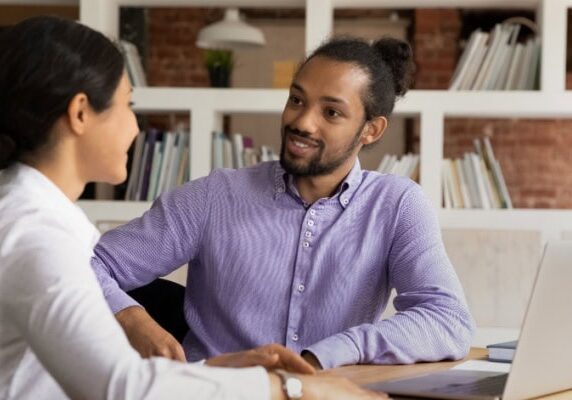 two people one coach one client seated in conversation at a table with a laptop