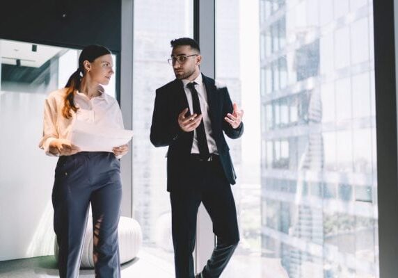 man and woman in business attire walking in a hallway engaged in conversation