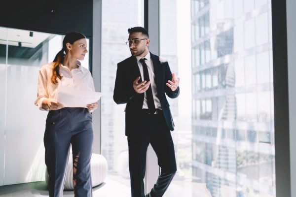 man and woman in business attire walking in a hallway engaged in conversation