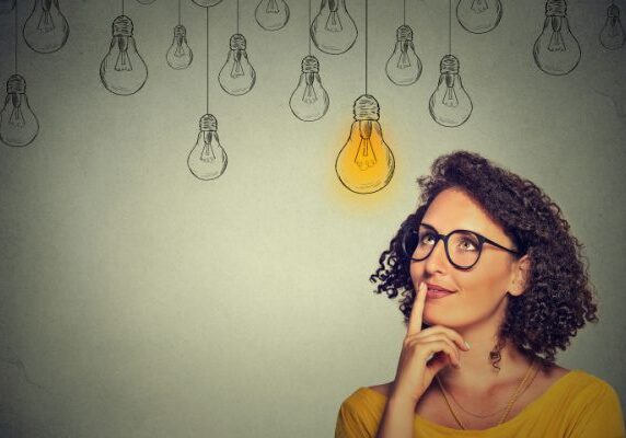 woman looking at light light bulb drawing hanging above her head with other unlit light bulb drawings also hanging