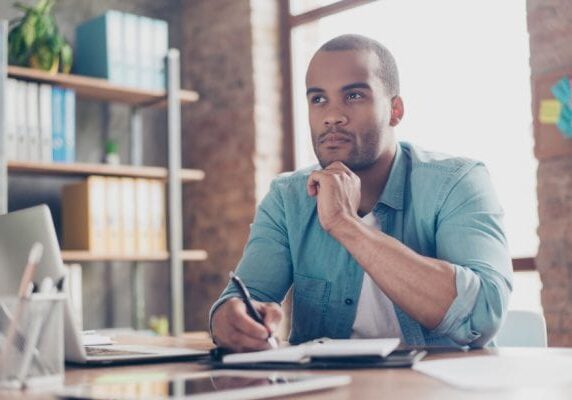 man looking curious and contemplative while writing in a notebook