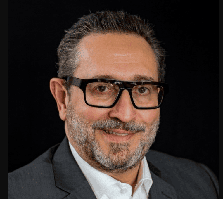 Joao Luiz Pasqual, MCC, headshot, a smiling man is wearing glasses and a button down white shirt with a suit jacket.