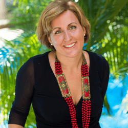 Gaelle Lecourt headshot photo, smiling woman with short blond hair wearing a black top and red necklace in front of tropical greenery